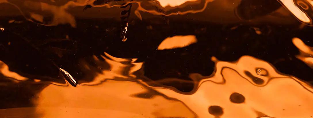 Bright orange liquid creates an abstract texture with rippling reflections and subtle light glimmers.