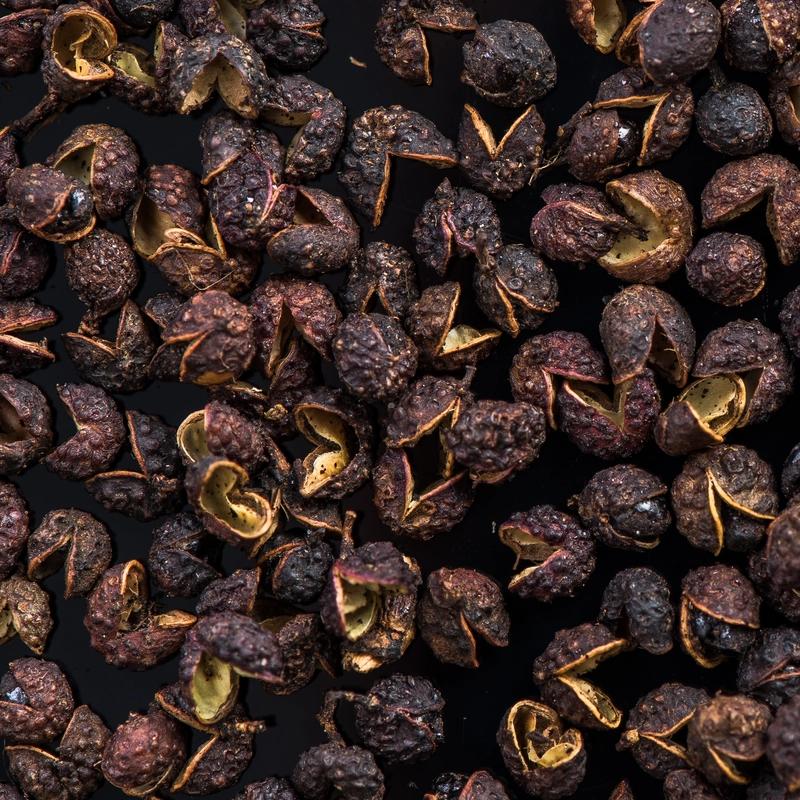 Overhead close-up of timur pepper scattered across a black background, revealing golden interiors; rustic, textural mood.
