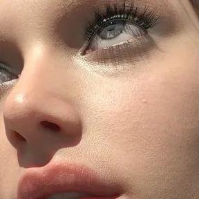 Close-up of a face with smooth, radiant skin, featuring long eyelashes and shimmering eyes. The complexion has a fresh and youthful appearance, conveying a serene mood.